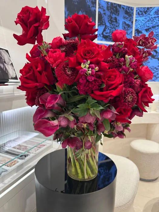 Corporate floral arrangement of deep red roses, dahlias and stock on a black plinth in a luxury boutique