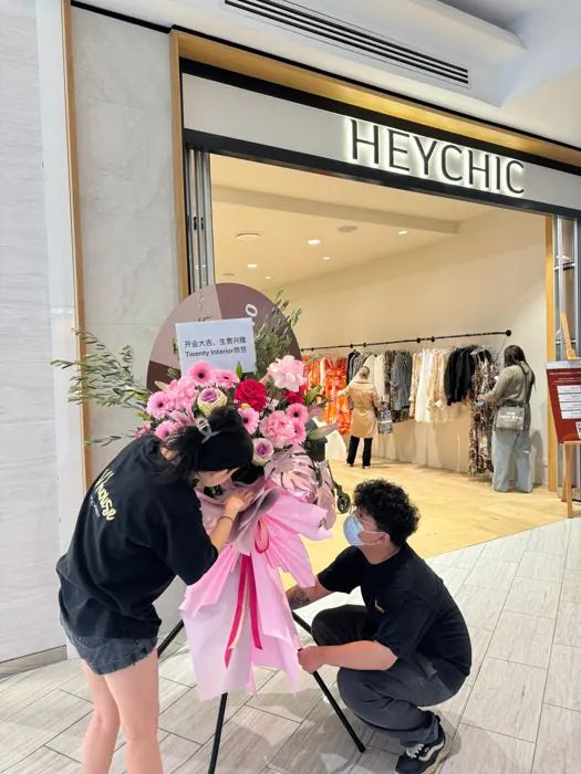 Vhouse Florist team setting up a grand-opening flower stand of pink gerberas and roses outside a new store