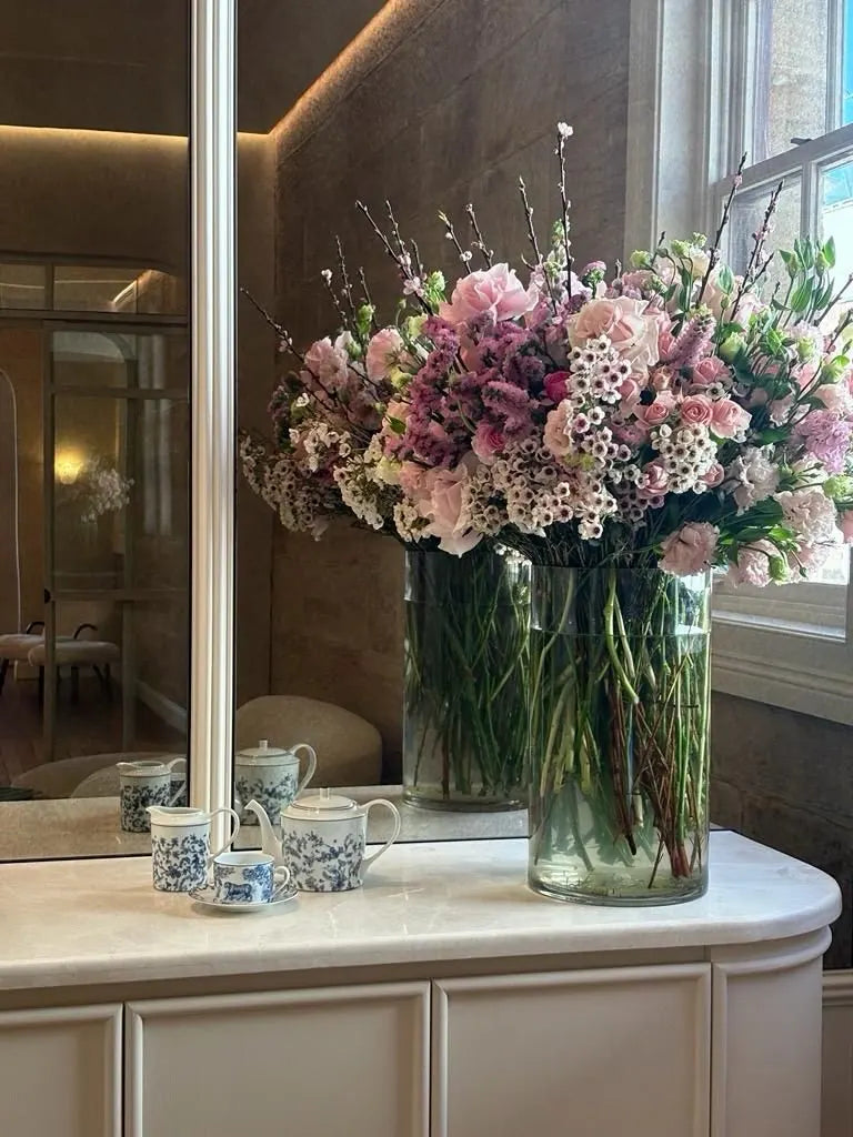 Front-of-house corporate flowers: two tall vases of blush roses, waxflower and cherry blossom on a marble console