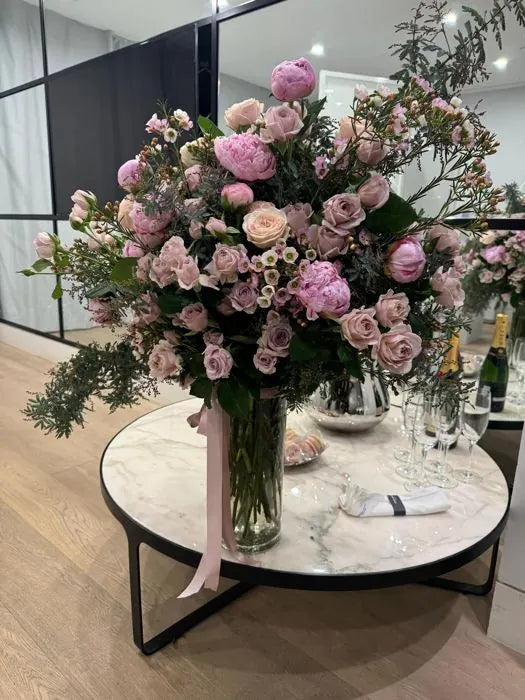 Corporate event flowers: pink roses, lisianthus and waxflower on a marble table set with champagne