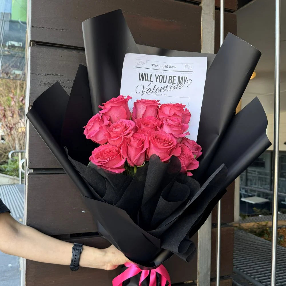 12 hot pink roses bouquet wrapped in black paper with pink ribbon held outdoors with romantic gift card, Sydney same-day luxury hot pink rose delivery by Vhouse Florist