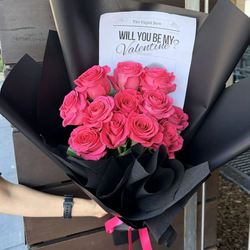 12 hot pink roses bouquet wrapped in black paper with romantic gift card held outdoors, Sydney same-day luxury hot pink rose delivery by Vhouse Florist