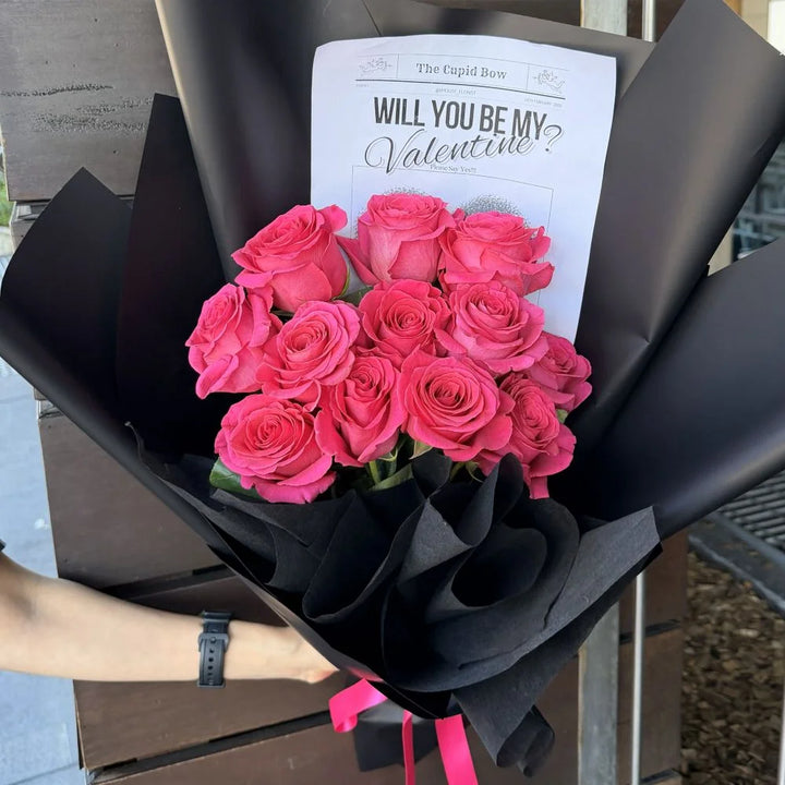12 hot pink roses bouquet wrapped in black paper with romantic gift card held outdoors, Sydney same-day luxury hot pink rose delivery by Vhouse Florist
