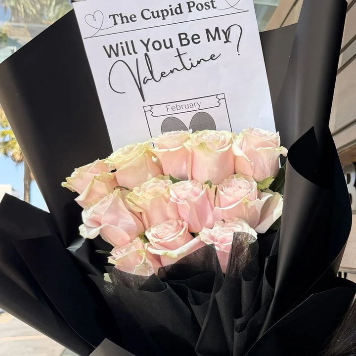 12 light pink roses bouquet in black paper with romantic gift card held outdoors in sunlight, Sydney same-day luxury light pink rose delivery by Vhouse Florist