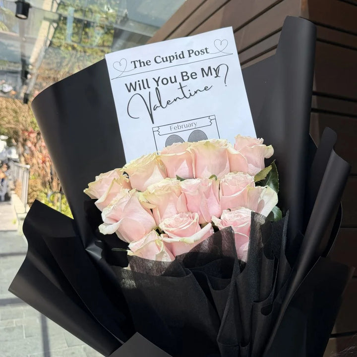 12 light pink roses bouquet wrapped in black paper with romantic gift card held outdoors, Sydney same-day luxury light pink rose delivery by Vhouse Florist