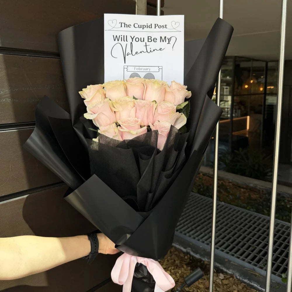 12 light pink roses bouquet wrapped in black paper with pink ribbon and romantic gift card held outdoors at night, Sydney same-day luxury light pink rose delivery by Vhouse Florist
