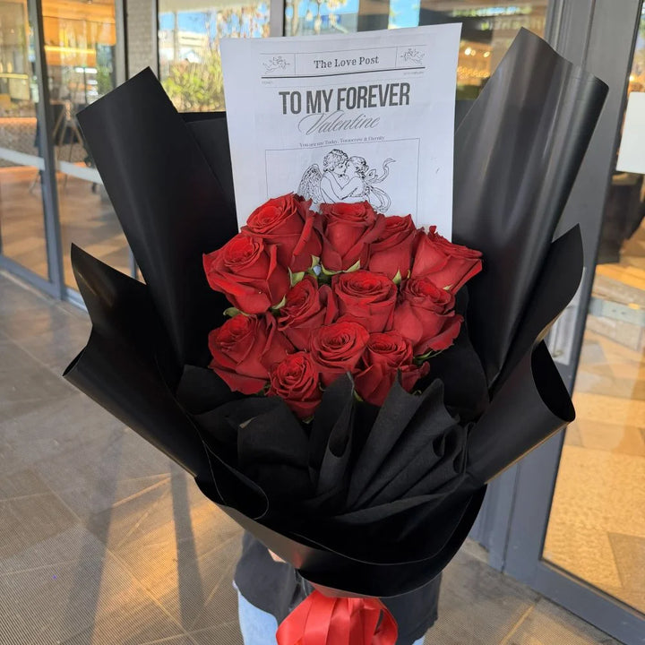 12 luxury red roses bouquet wrapped in black paper with romantic gift card held outdoors, Sydney same-day luxury red rose delivery and romantic flower gifts by Vhouse Florist