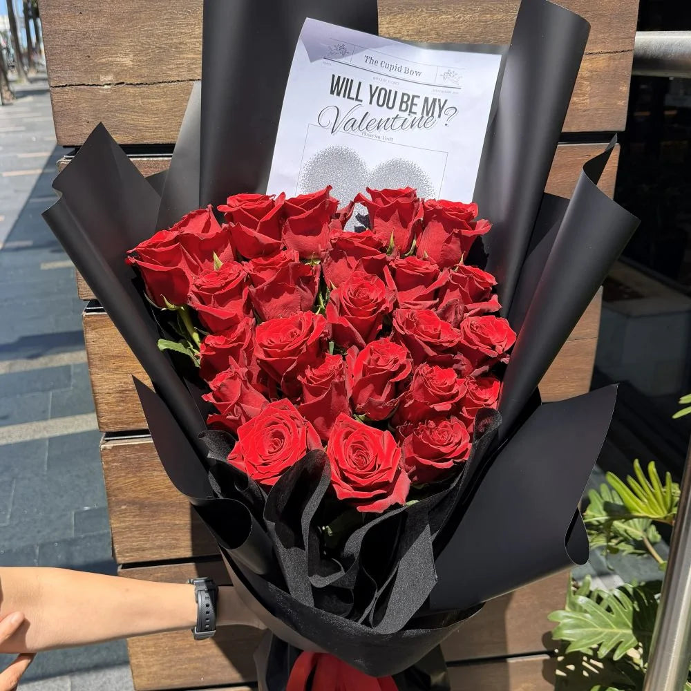 24 luxury red roses bouquet wrapped in black paper held outdoors with romantic gift card, Sydney same-day luxury red rose delivery by Vhouse Florist