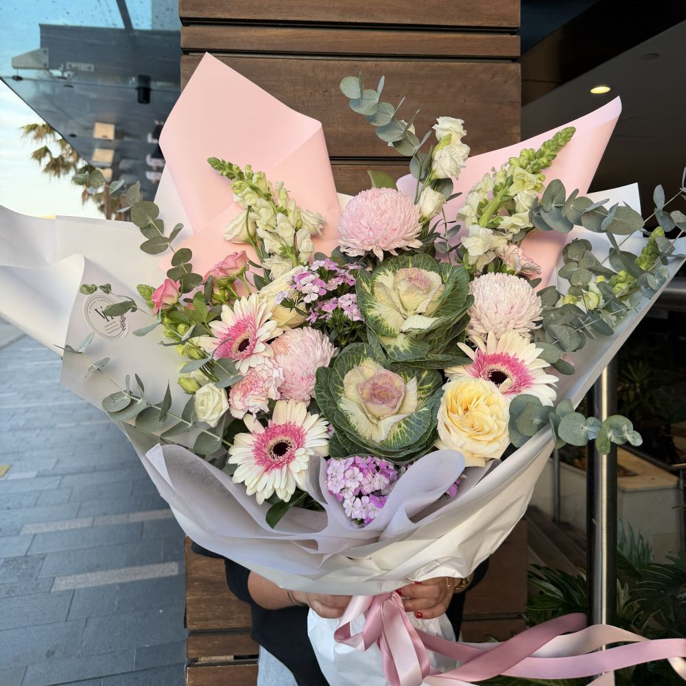 Vhouse Florist luxury pink bouquet with gerberas, ornamental kale, pink chrysanthemums and eucalyptus held outdoors wrapped in pink paper, Sydney same-day luxury flower delivery