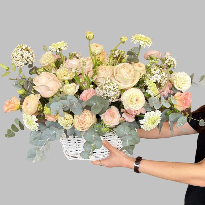 Light pastel flowers arranged in a white bamboo basket