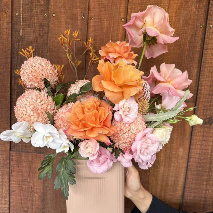 Autumn Blaze - orange, light pink and white flowers in a pastel pink ceramic vase, hand-held view