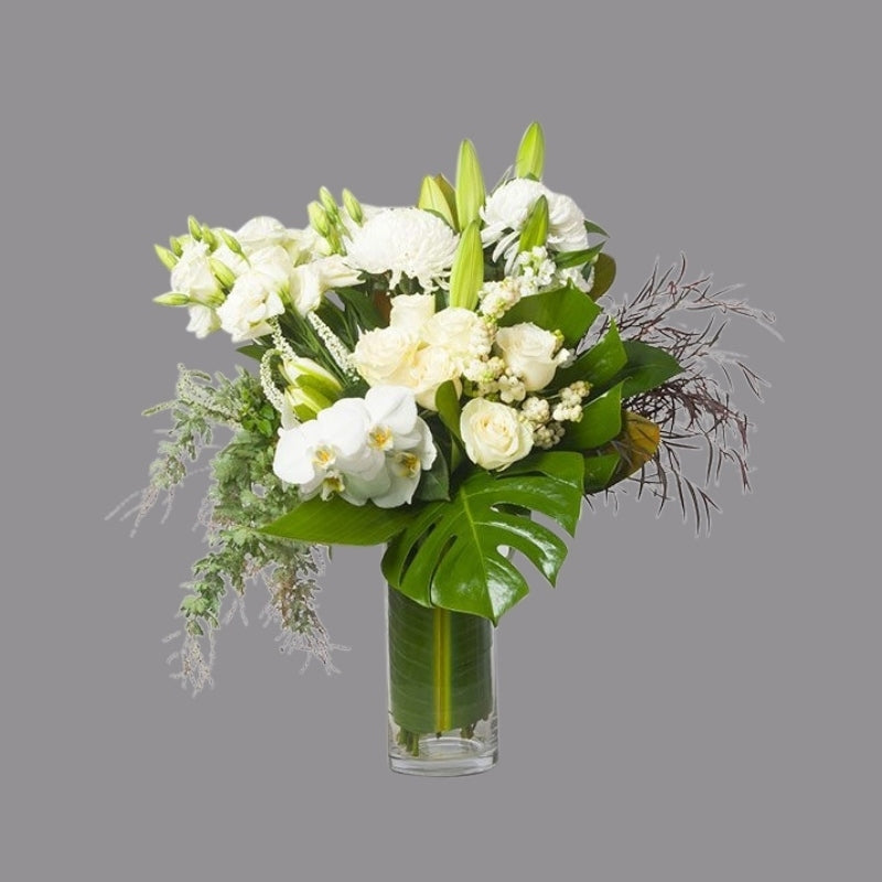 White flowers with greenery in cylindrical glass vase