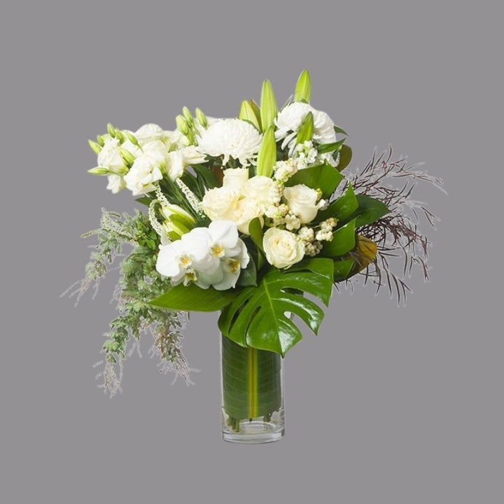 White flowers with greenery in cylindrical glass vase