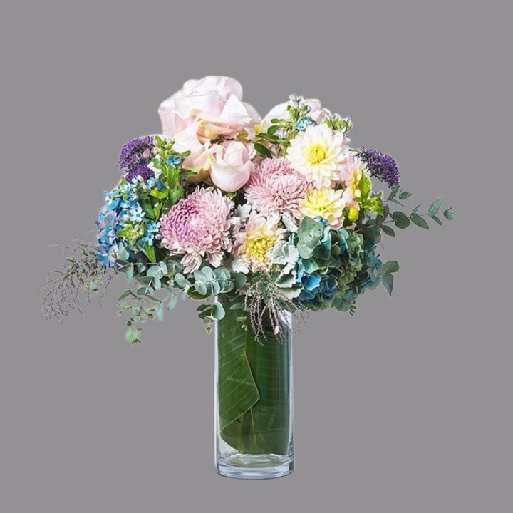 Luxury bouquet of hydrangea, soft pink roses, dusty miller, ast foliage, and texture in cylindrical glass vase.