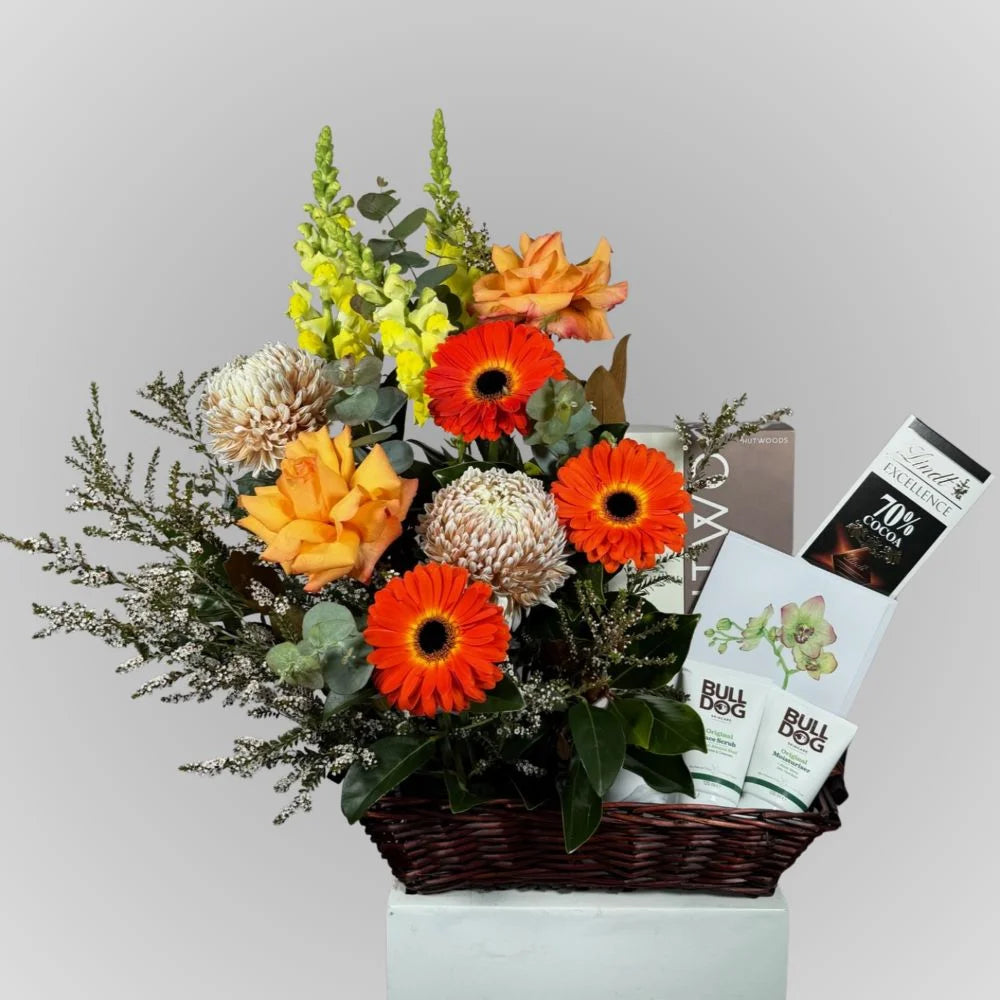 Men's gift hamper in a dark brown wicker basket with orange gerbera daisies, yellow-orange roses, cream chrysanthemums, eucalyptus, Bulldog treats and a gift box—ideal for Father's Day or a boyfriend's birthday.