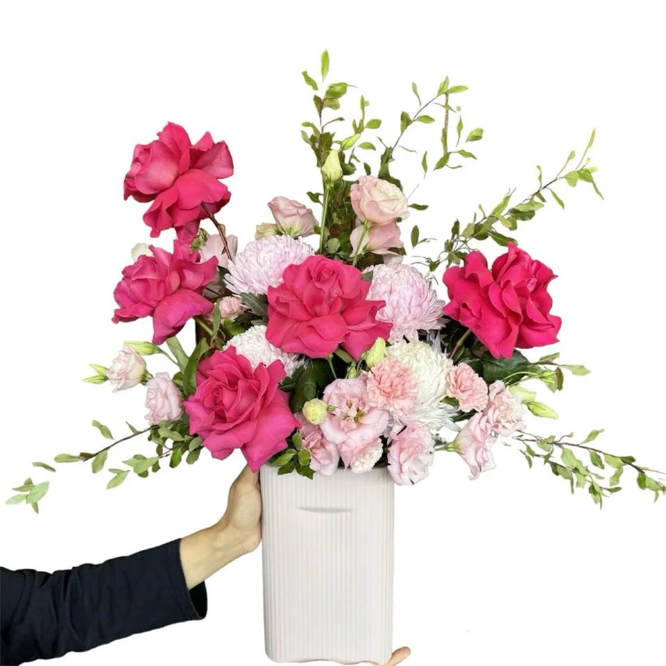 Pink roses and light Pink Flowers with greenery in white straight ceramic vase, hand-held view