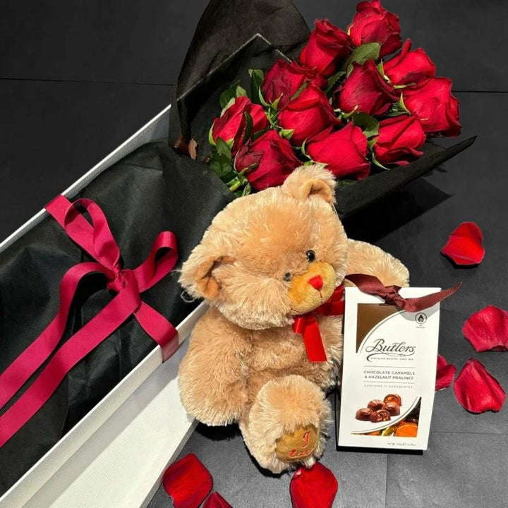 Luxury romantic gift set with red roses in black wrap, teddy bear and chocolates on dark background with rose petals, Sydney same-day luxury flower and gift delivery by Vhouse Florist