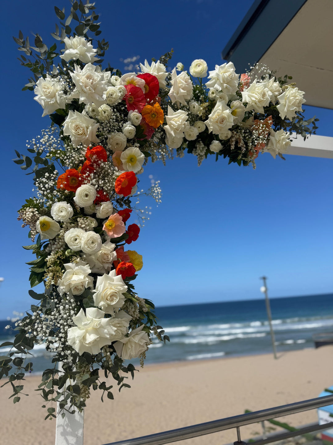 Beachfront wedding ceremony arch with white roses and poppies by Vhouse Florist