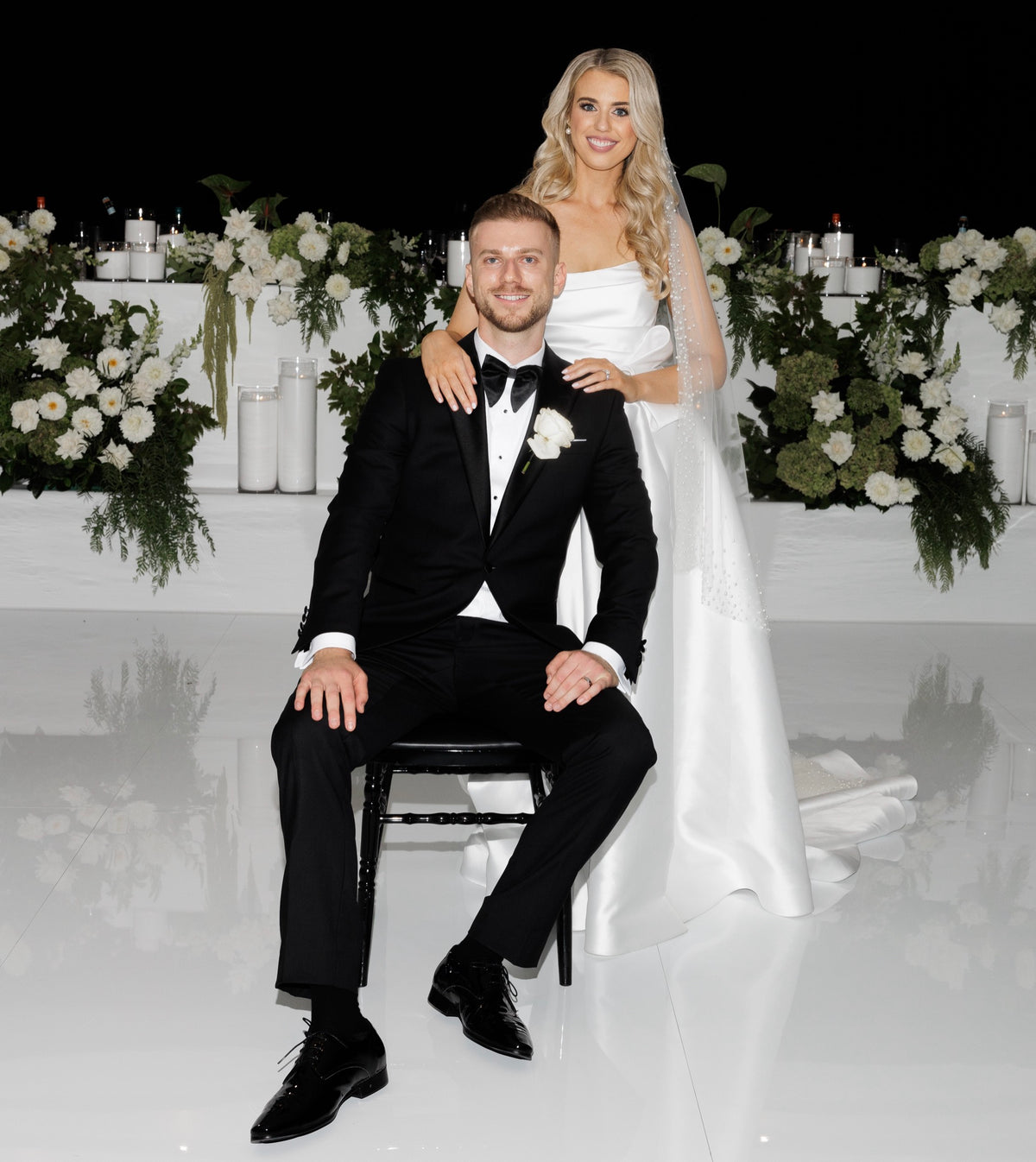Bride and groom seated among white wedding flowers and candles styled by Vhouse Florist