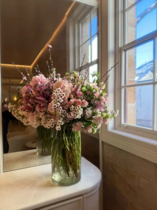 Reception console flowers: blush roses, purple statice and waxflower in a glass vase by a window