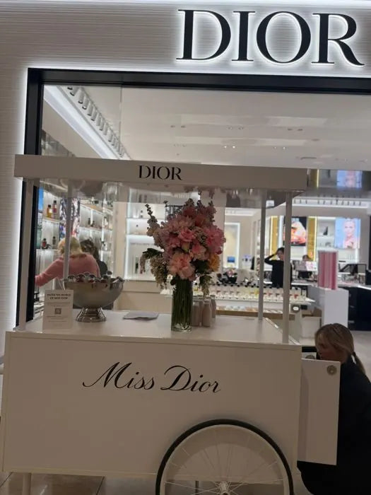 Pop-up event flowers: pink and peach roses with stock in a tall vase on a Miss Dior cart outside a Dior boutique