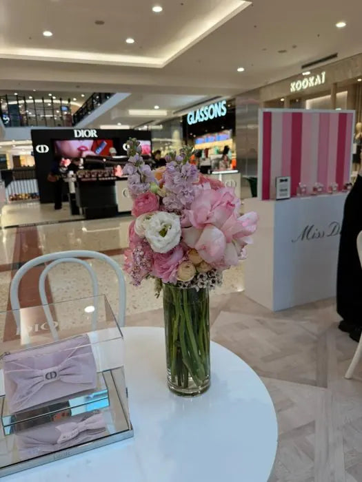 Pop-up table flowers: pink roses, stock and waxflower in a glass vase at a Miss Dior pop-up in a Sydney shopping centre