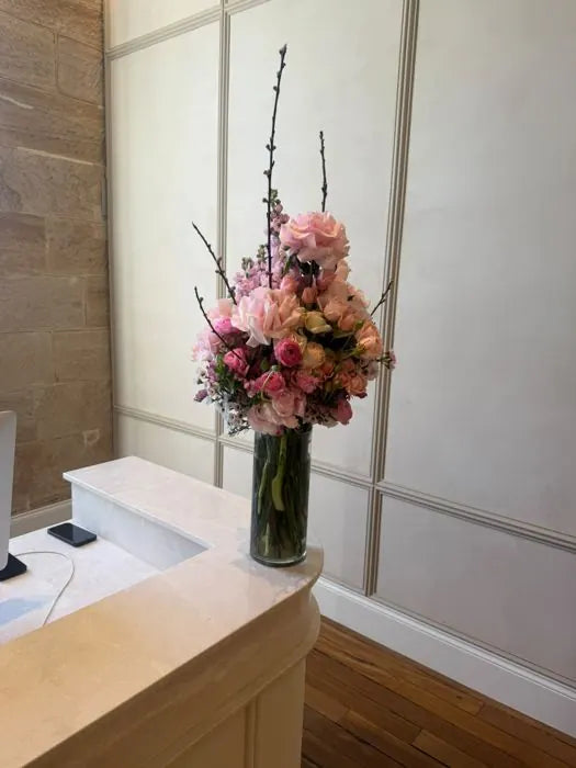 Office flowers for a front desk: pink roses and cherry blossom in a tall glass vase
