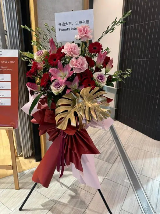 Grand-opening flower stand with red roses, pink carnations, lilies and gold monstera leaves for a shop opening