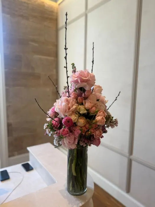 Reception flowers for a Sydney office: pink roses and blossom branches in a glass vase on a stone desk